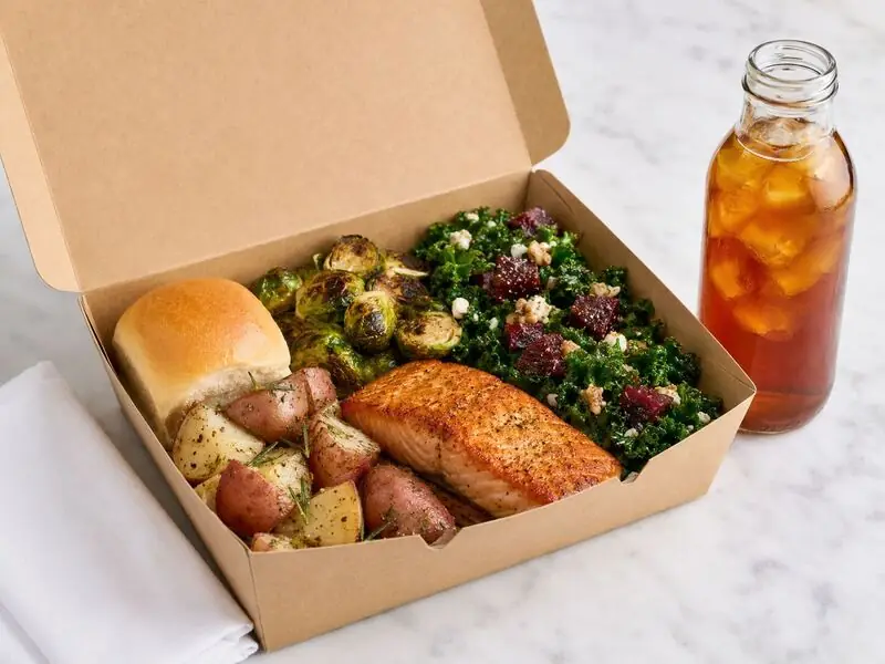 Individually packed boxed meal of baked salmon, rosemary potatoes, Brussels sprouts, kale salad, and iced tea for a Peninsula office lunch