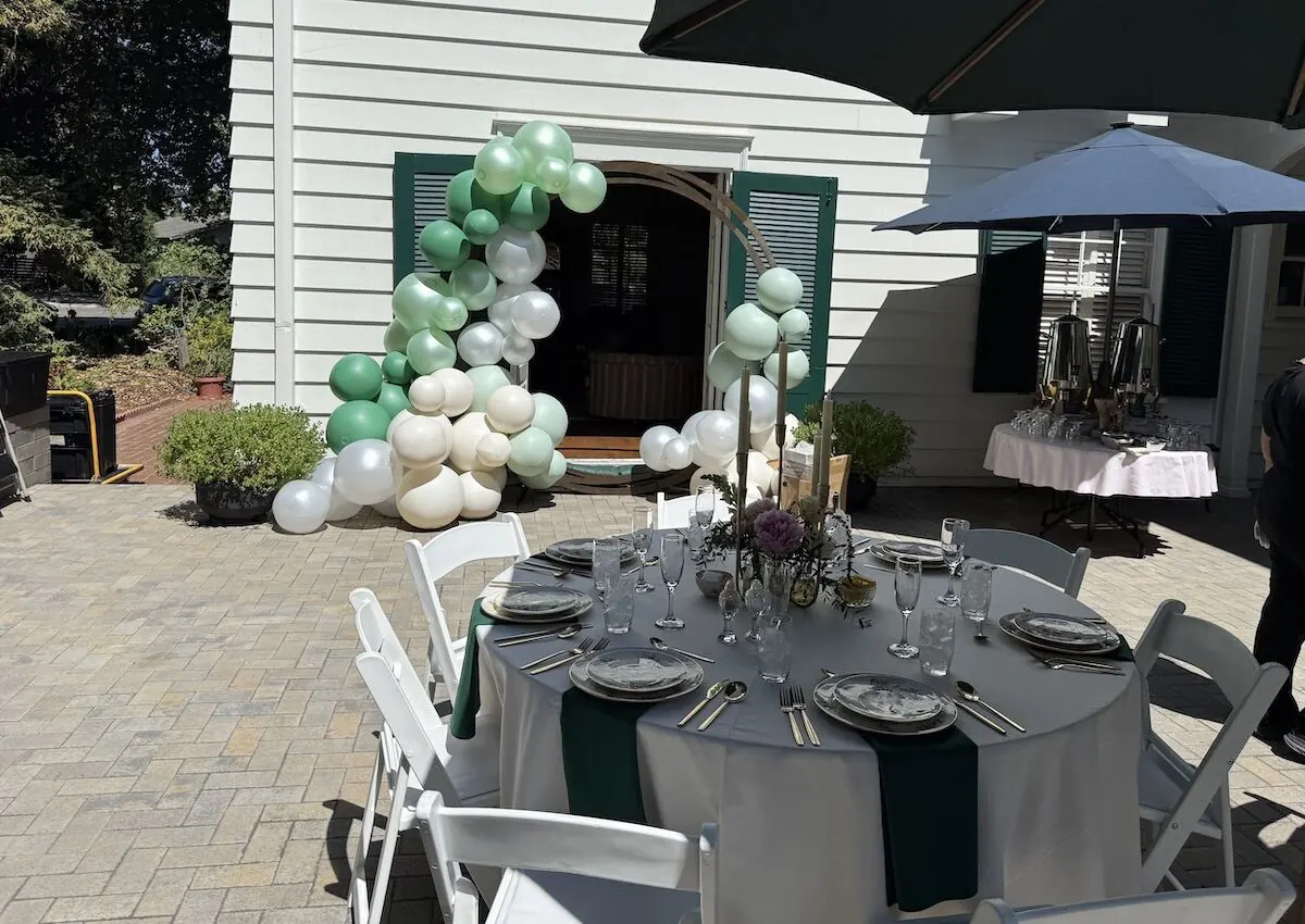 Sage and ivory balloon garland arcing across a doorway beside a fully styled table