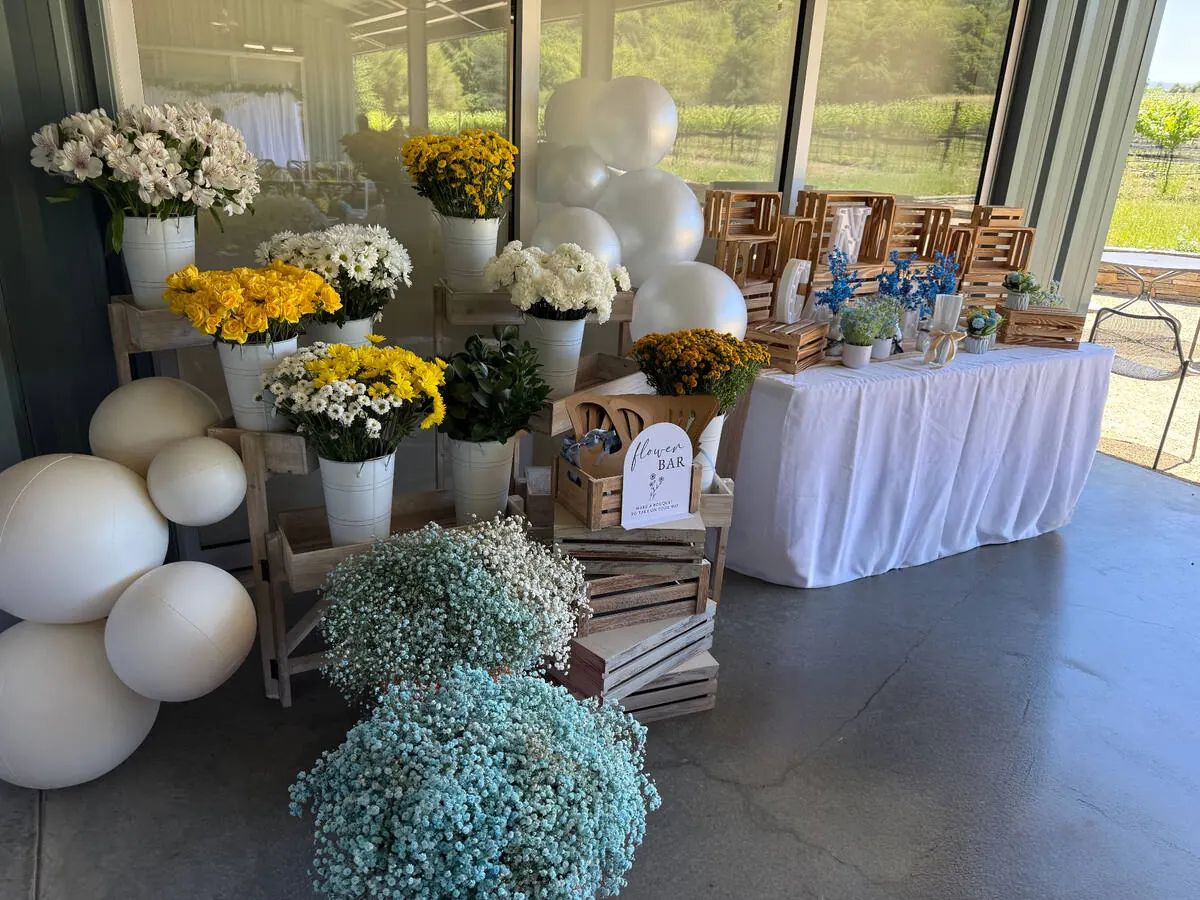 Bloom bar stocked with yellow roses, daisies and baby's breath beside ribbon and wrapping paper for guests