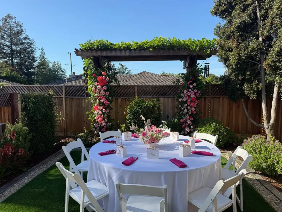 Rose arch bending over a garden round set in crisp white cloth with fuchsia napkins folded at each seat