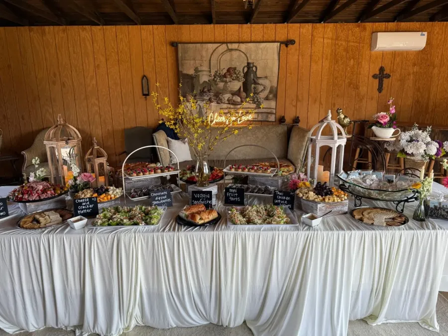 Grazing tablescape stacked with charcuterie, tea sandwiches, glazed tarts and chilled salads across layered linens